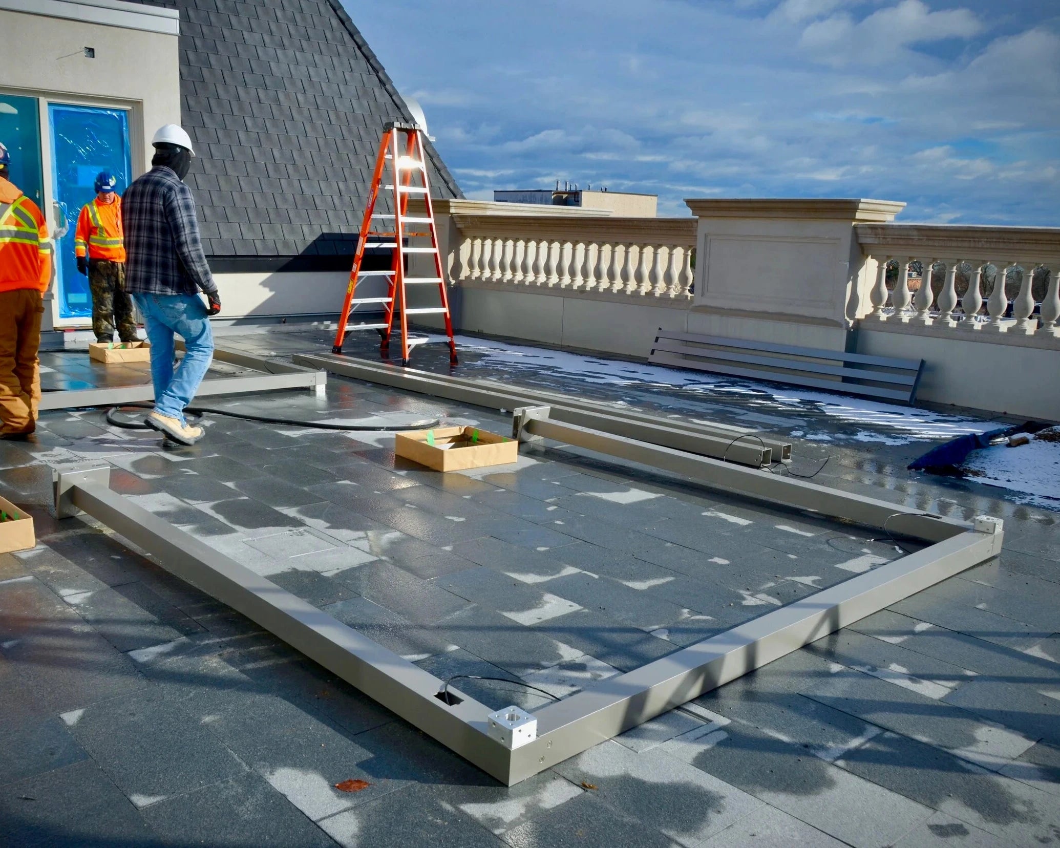 Construction workers on a rooftop installing a metal structure with a clear sky in the background.